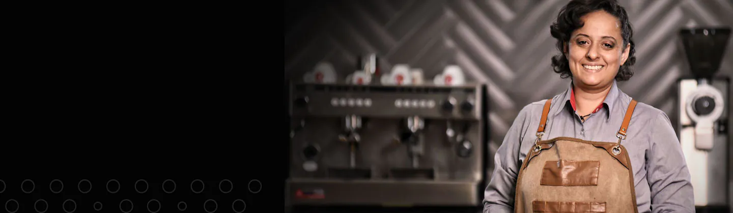 Uma barista sorrindo com uma máquina de café no fundo